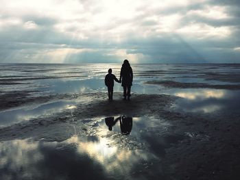 Silhouette friends standing on beach against sky during sunset