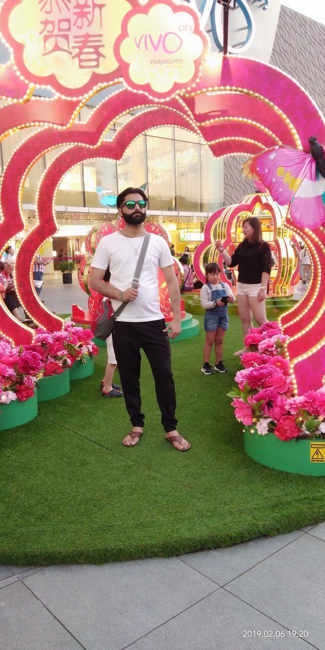 REAR VIEW OF PEOPLE STANDING BY FLOWERS