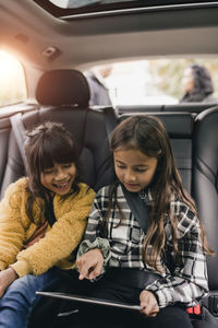 Sisters using digital tablet while sitting in car