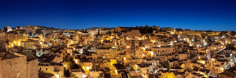 Panoramic view of illuminated buildings against clear blue sky at night