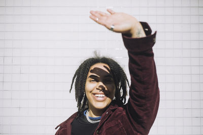 Portrait of cheerful non-binary person shielding eyes while standing against wall