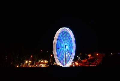 Illuminated ferris wheel against sky in city at night