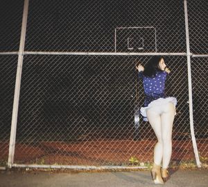 Rear view of woman standing by chainlink fence