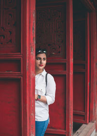 Portrait of young woman standing against red door