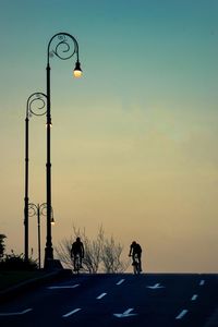 Silhouette people riding bicycles on road against sky during sunset