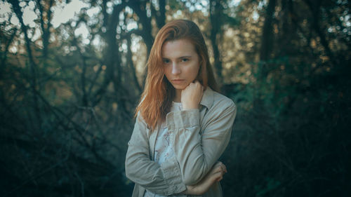 Portrait of young woman standing against trees