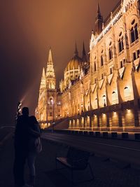 Rear view of man and illuminated buildings in city at night