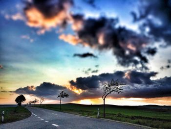 Road passing through field against cloudy sky