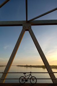 Bicycle by railing against sky during sunset