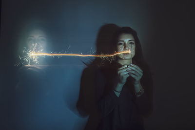 Multiple image of woman holding illuminated sparklers at night