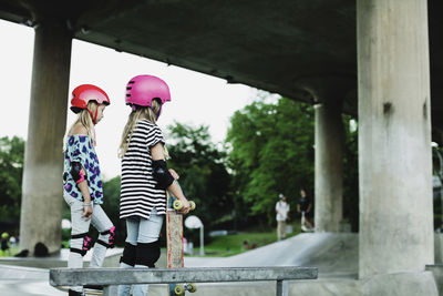 Friends wearing helmets and safety pads standing at skateboard park