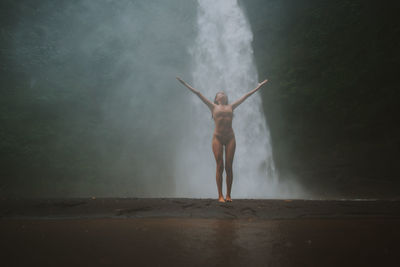 Young woman standing against waterfall