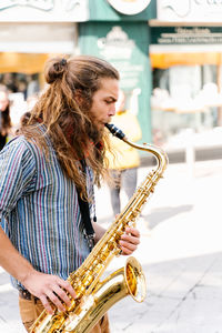 Portrait of a young man with long hair playing saxophone in the street
