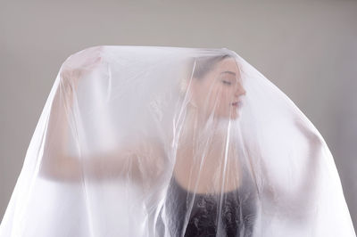 Young woman holding plastic while standing against wall