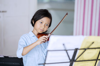 Cute girl playing violin with musical note on stand in foreground