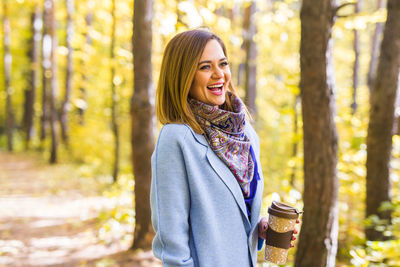 Smiling young woman standing against trees in forest