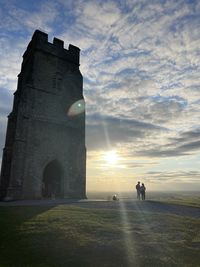 People by historic building against sky during sunset