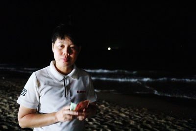 Portrait of young man looking at beach against sky at night