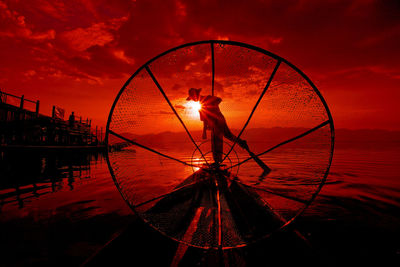 Fisherman standing on boat seen through fishing net during sunset