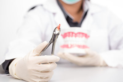 Midsection of dentist holding tooth on pliers in clinic