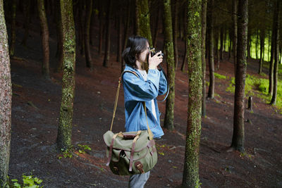 Standing by tree trunk in forest,shooting,cameraman