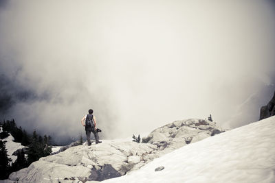 Rear view of man standing on mountain during foggy weather