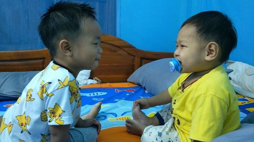 Side view of cute sibling looking at each other while sitting on bed