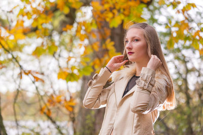 Beautiful woman holding her hair while standing at park during autumn