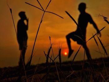 Silhouette people on field against orange sky