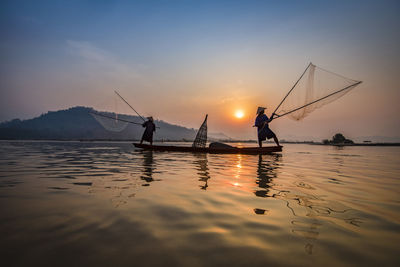 Silhouette people fishing in sea against sky during sunset