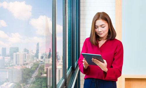 Young woman looking through smart phone while sitting on window