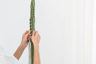 Handmade green macrame plant hangers with potted plant are hanging on woman hand. pot and monstera