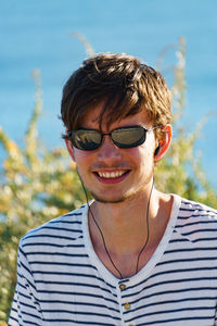 Close-up of man wearing sunglasses while listening music against plants on sunny day