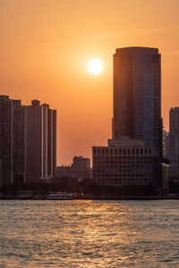 Modern buildings by sea against sky during sunset