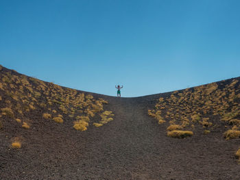 Distant view of mature woman standing on mountain against clear blue sky