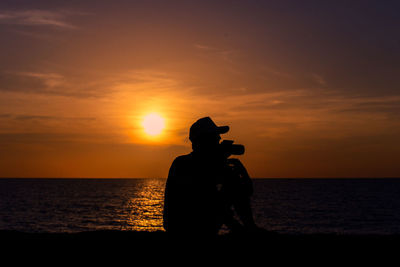 Silhouette man with camera against sky during sunset