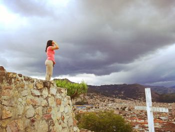 Side view of woman standing on retaining wall against sky