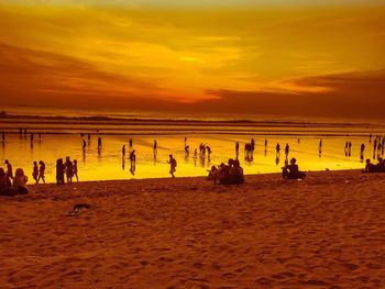 Silhouette people on beach against cloudy sky during sunset