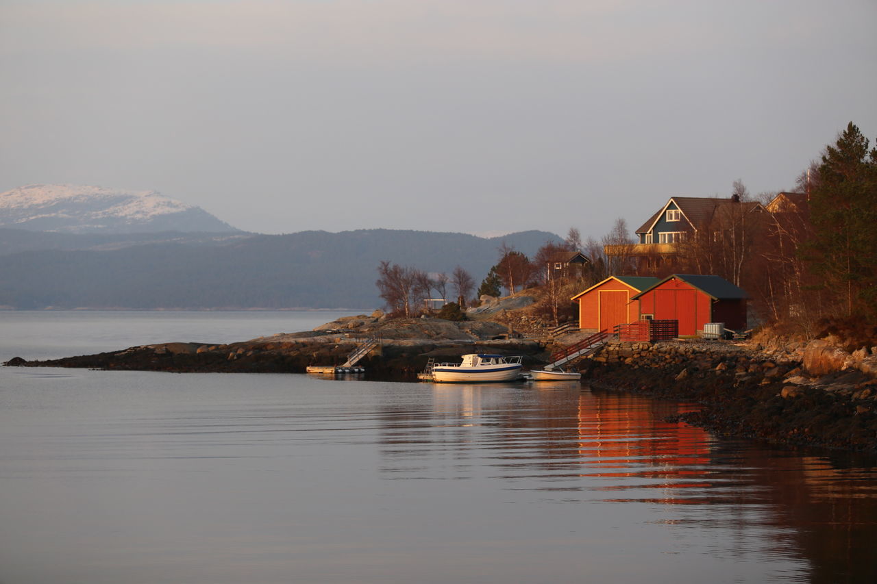 water, waterfront, mountain, lake, built structure, architecture, tranquil scene, building exterior, house, tranquility, scenics, reflection, sky, nature, clear sky, beauty in nature, nautical vessel, tree, river, boat