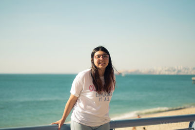 Portrait of beautiful woman standing by sea against sky