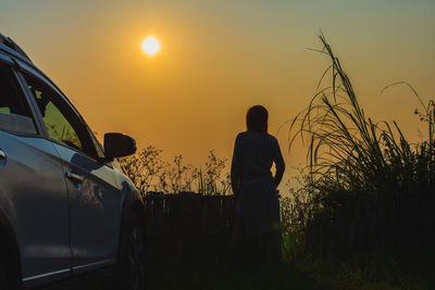 Silhouette man standing by car against sky during sunset
