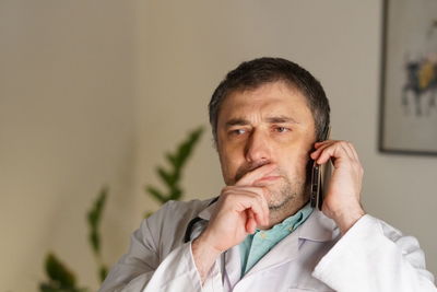 Mature doctor using phone against wall