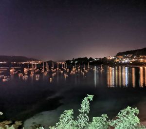 Illuminated city by lake against sky at night