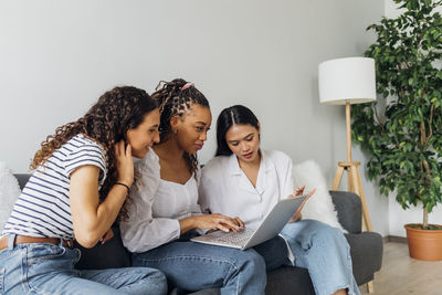 Woman doing online shopping on laptop with friends in living room