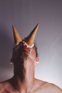 Close-up of shirtless man with ice cream cones on eyes against wall