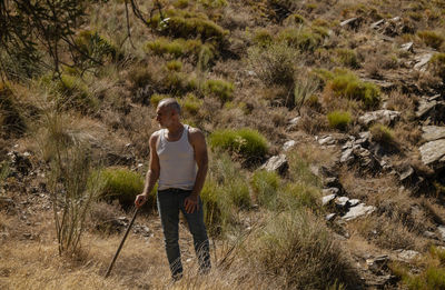 Adult man in white tank top and jeans working on field in summer