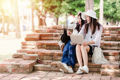 Full length of woman using mobile phone while sitting on staircase