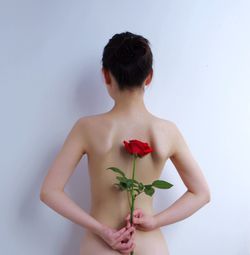 Rear view of naked woman holding rose and standing against white background
