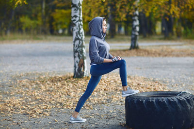 A brunette girl in a tracksuit performs morning sports exercises on the street on the beach.