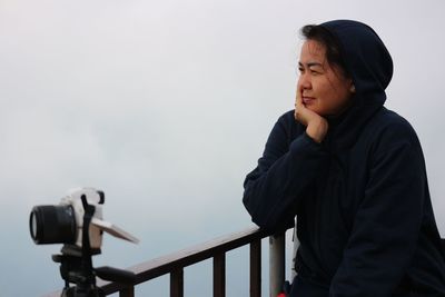 Smiling woman looking at view while sitting by railing against sky